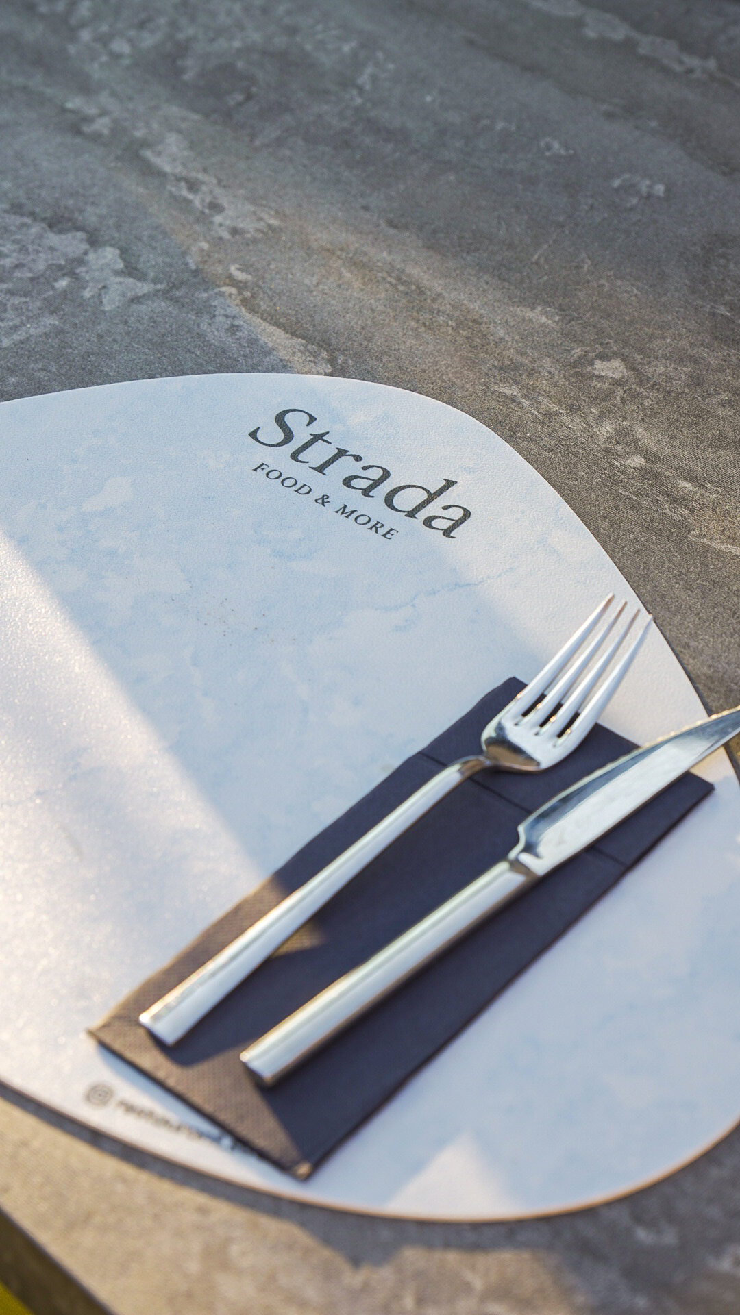 A Strada table setting with menu and cutlery in afternoon light